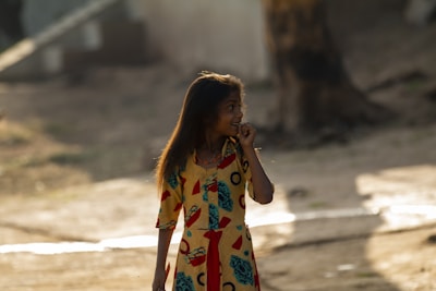 Young girl wearing a fashionable outfit posing in a sunny outdoor setting.