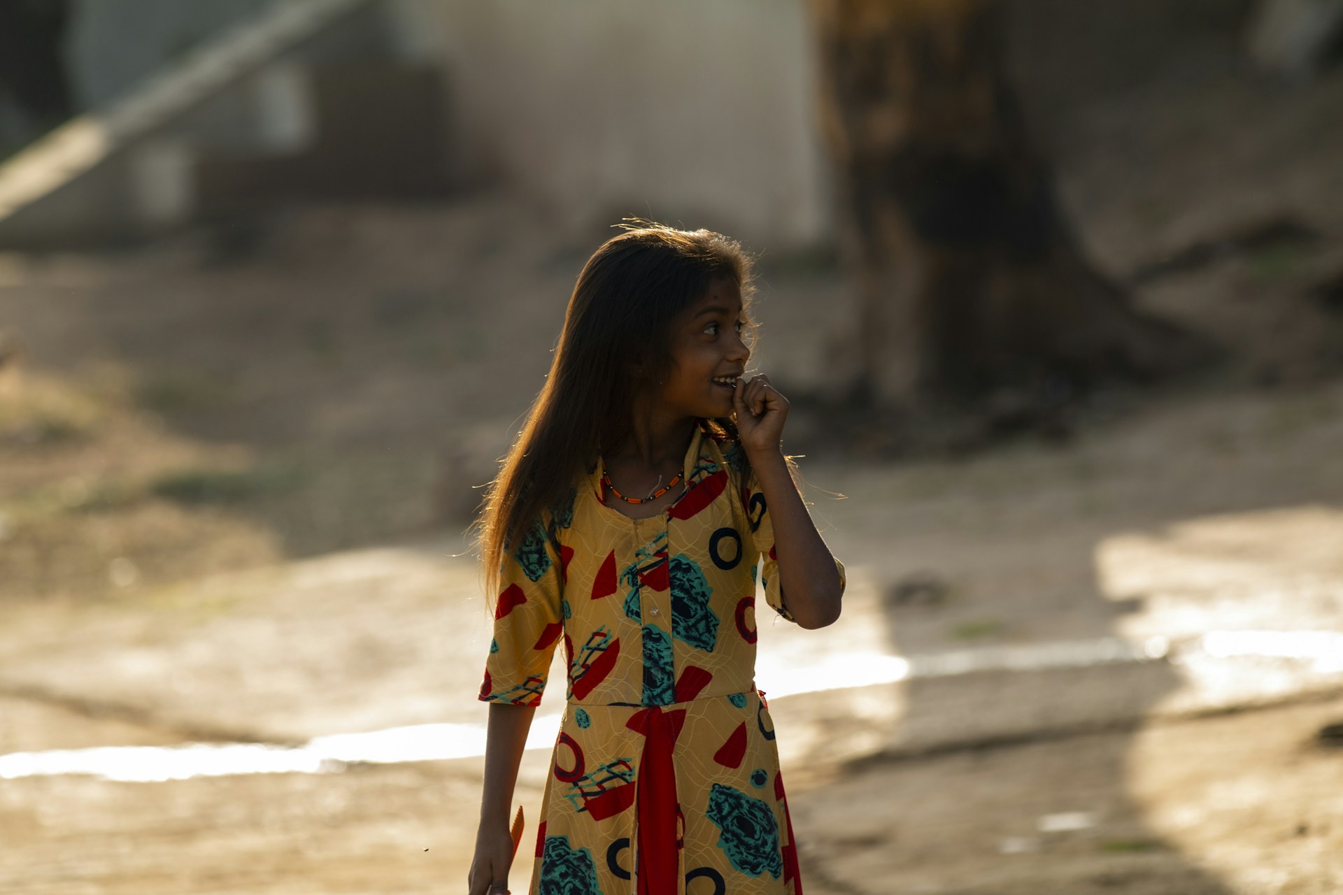 A young girl wearing a colorful summer dress smiling outdoors in natural light