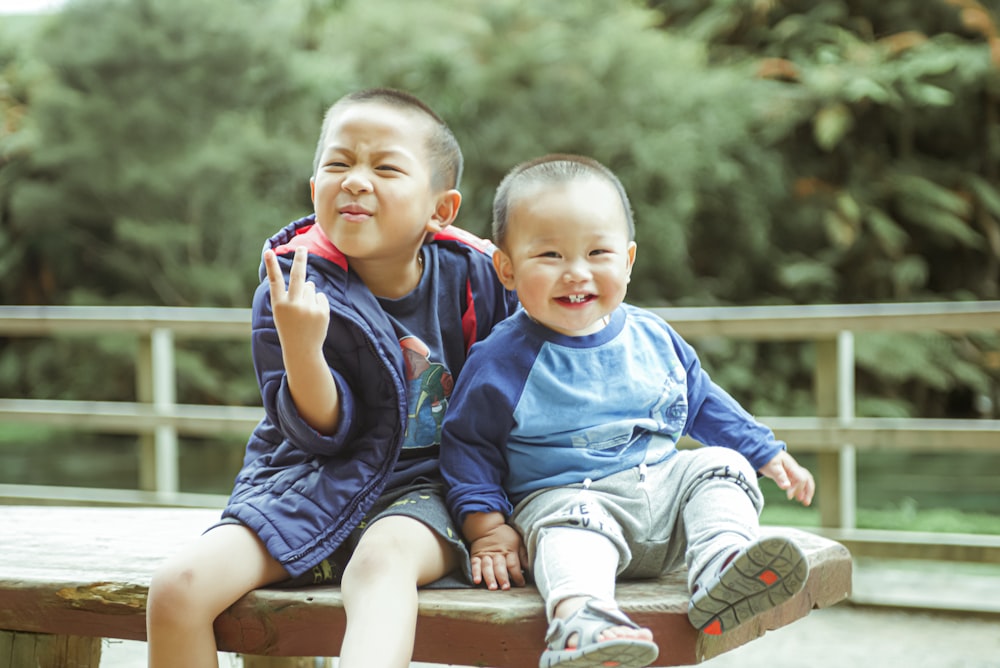 boy in blue long sleeve shirt sitting on brown wooden bench