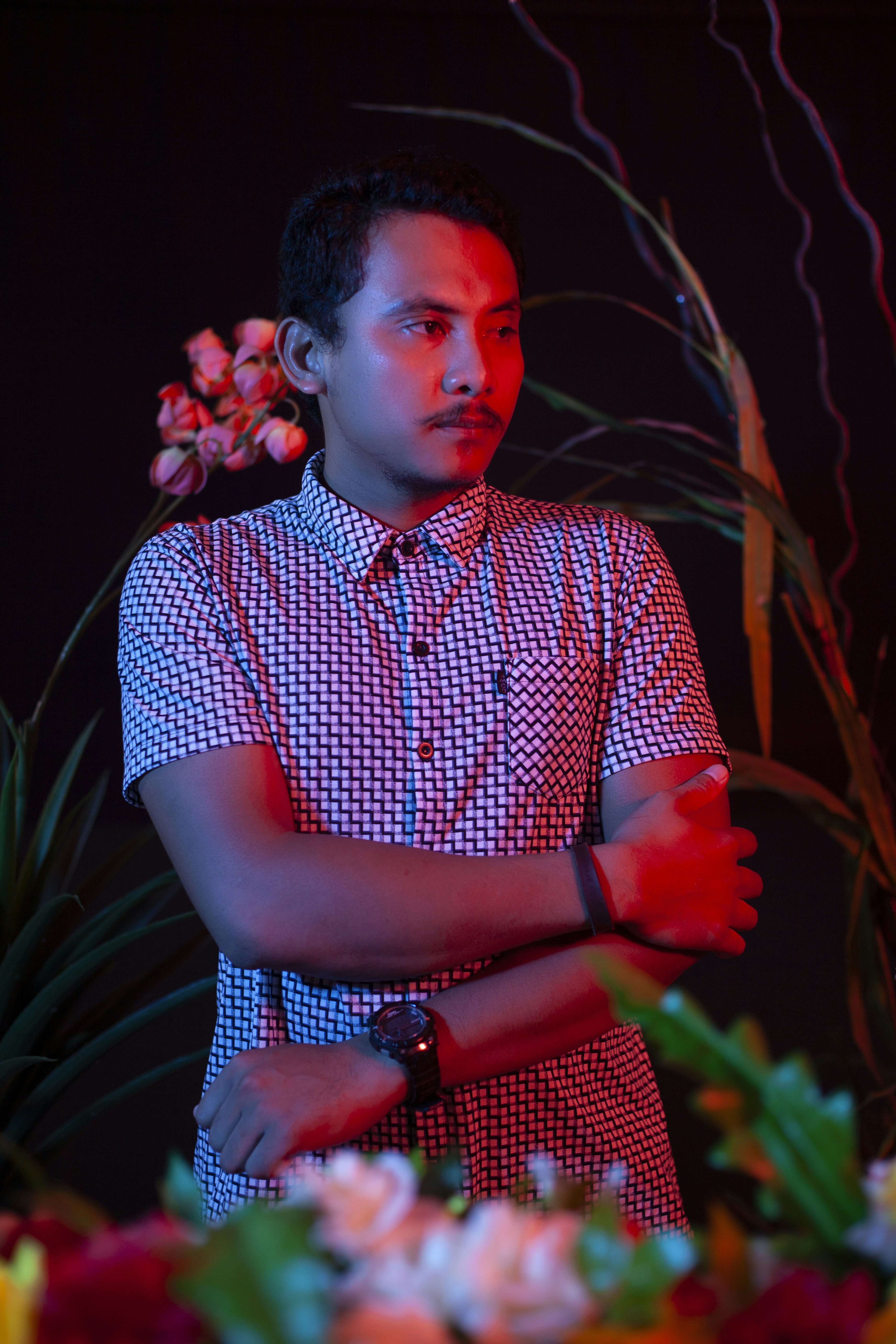 man in blue and white checkered button up shirt standing near red flowers