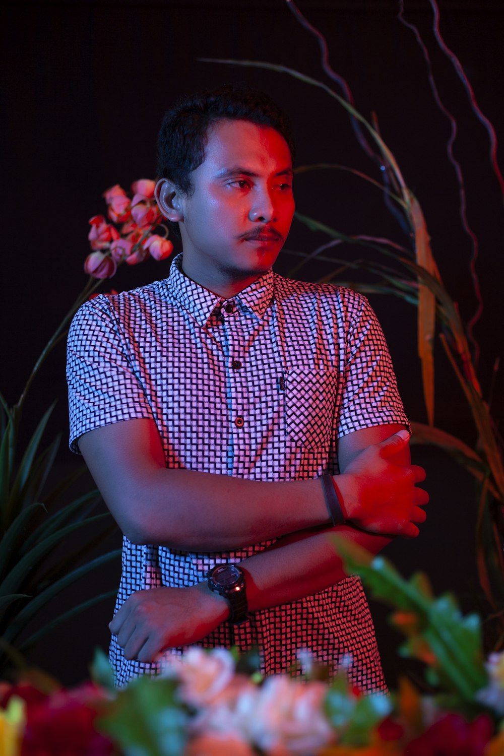 man in blue and white checkered button up shirt standing near red flowers