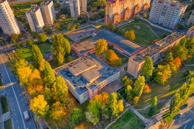 Aerial view of a residential area with several multi-story apartment buildings, surrounded by green spaces and trees with autumn foliage. The buildings have light-colored exteriors, and the area also includes roads, sidewalks, and recreational areas.