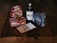 A collection of Swedish food items is arranged on a rustic wooden table. It includes a bag of gifflar pastries, a box of Annas Original Ginger Thins, a bottle of Skånska Spritfabriken cherry cordial, a box of Leksands Crispbread, and a small packet of snack mix.