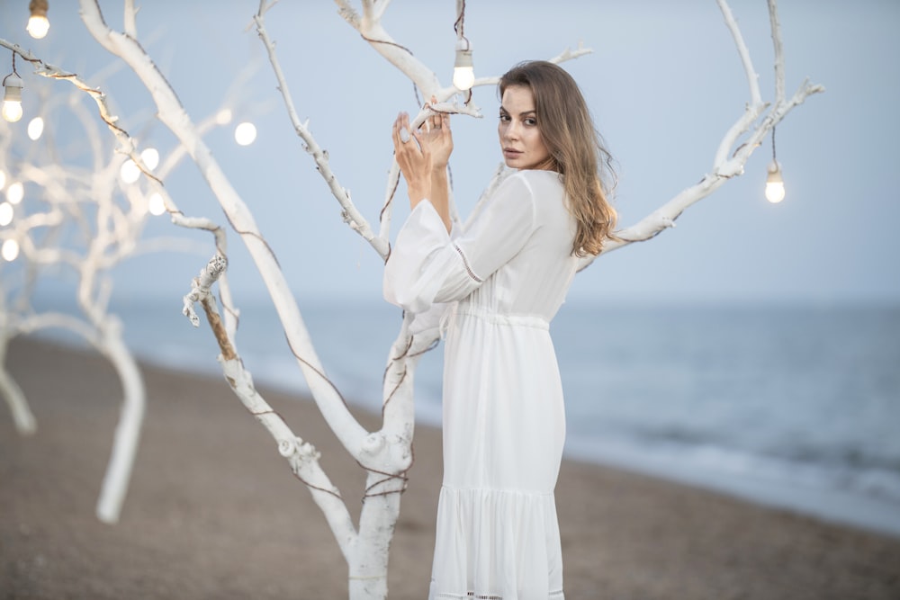 woman in white long sleeve dress holding white string lights