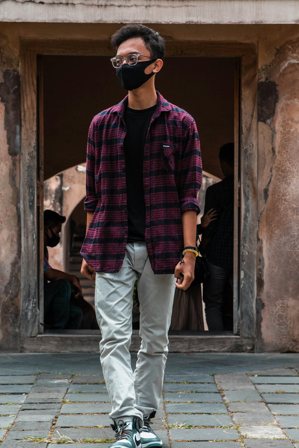 man in red and black plaid button up shirt and white pants standing beside brown concrete