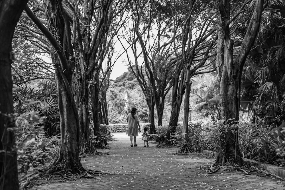 grayscale photo of couple walking on pathway between trees