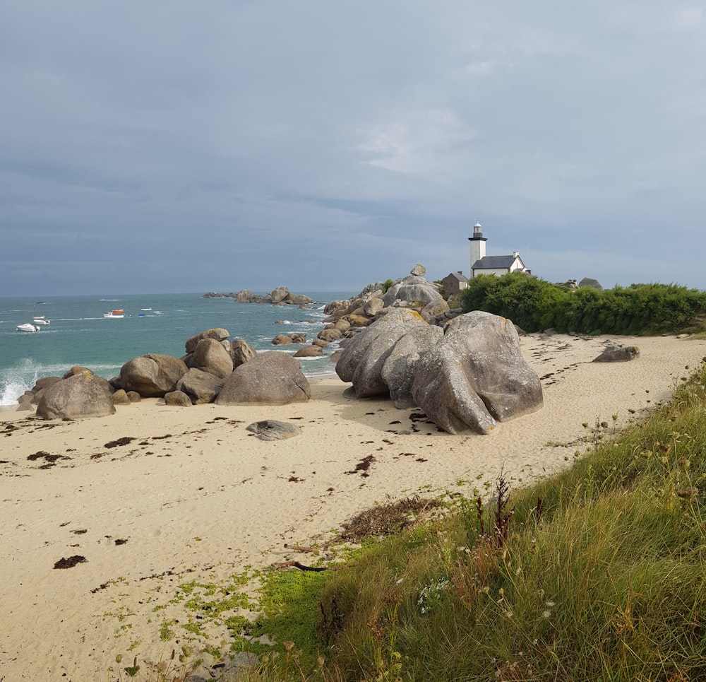 Phare blanc sur une formation rocheuse grise près d’un plan d’eau pendant la journée