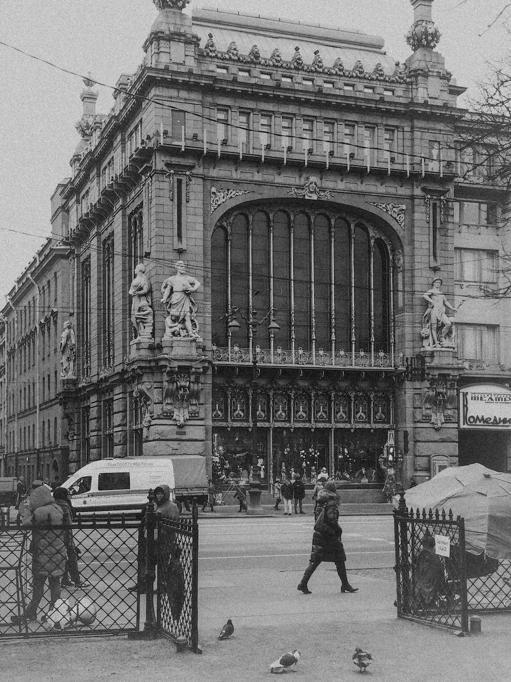 grayscale photo of man walking on sidewalk near building