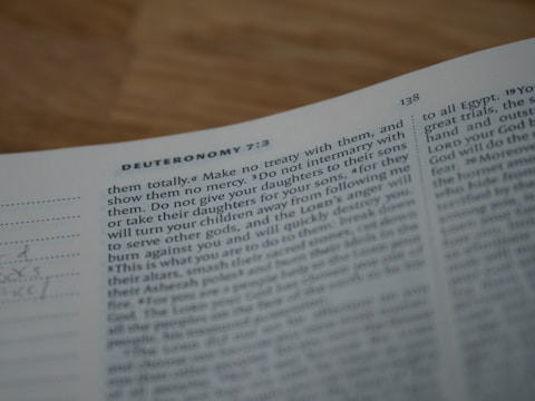 A close-up of an open book focusing on a passage from Deuteronomy 7:3-4. The text appears typed in a standard font and is slightly out of focus.