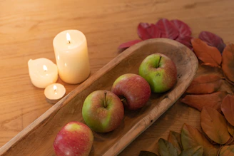 A rustic wooden table displaying a cinnamon-spiced candle with autumn leaves scattered around.