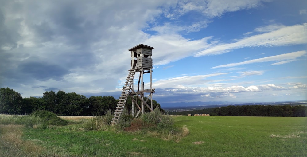 Brauner Holzturm auf grünem Rasenfeld unter blauem Himmel und weißen Wolken tagsüber