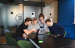 Students and academics engaged in a lively discussion around a laptop in a bright, modern study space.