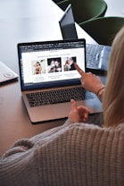 A person wearing a gray sweater is pointing to a laptop screen displaying a web page. The webpage contains a header titled 'Inspiration and Opportunities You Can't Miss' and features three sections with images and text. Nearby, there is another laptop on the table.