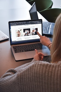 A person wearing a gray sweater is pointing to a laptop screen displaying a web page. The webpage contains a header titled 'Inspiration and Opportunities You Can't Miss' and features three sections with images and text. Nearby, there is another laptop on the table.