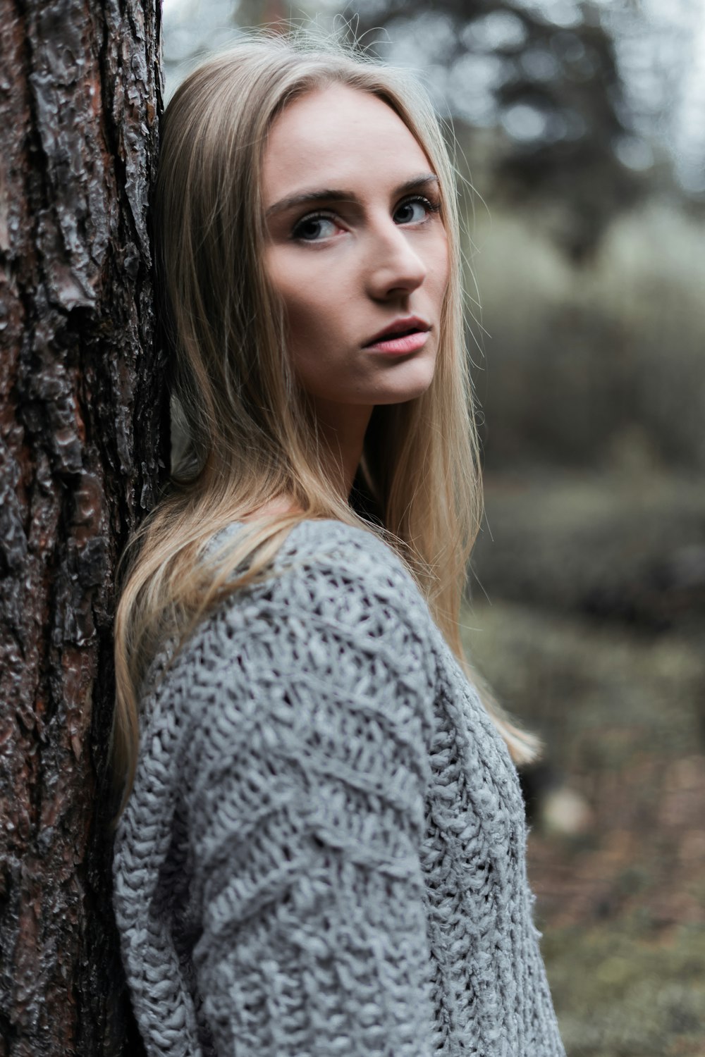 woman in gray knit sweater standing beside brown tree during daytime