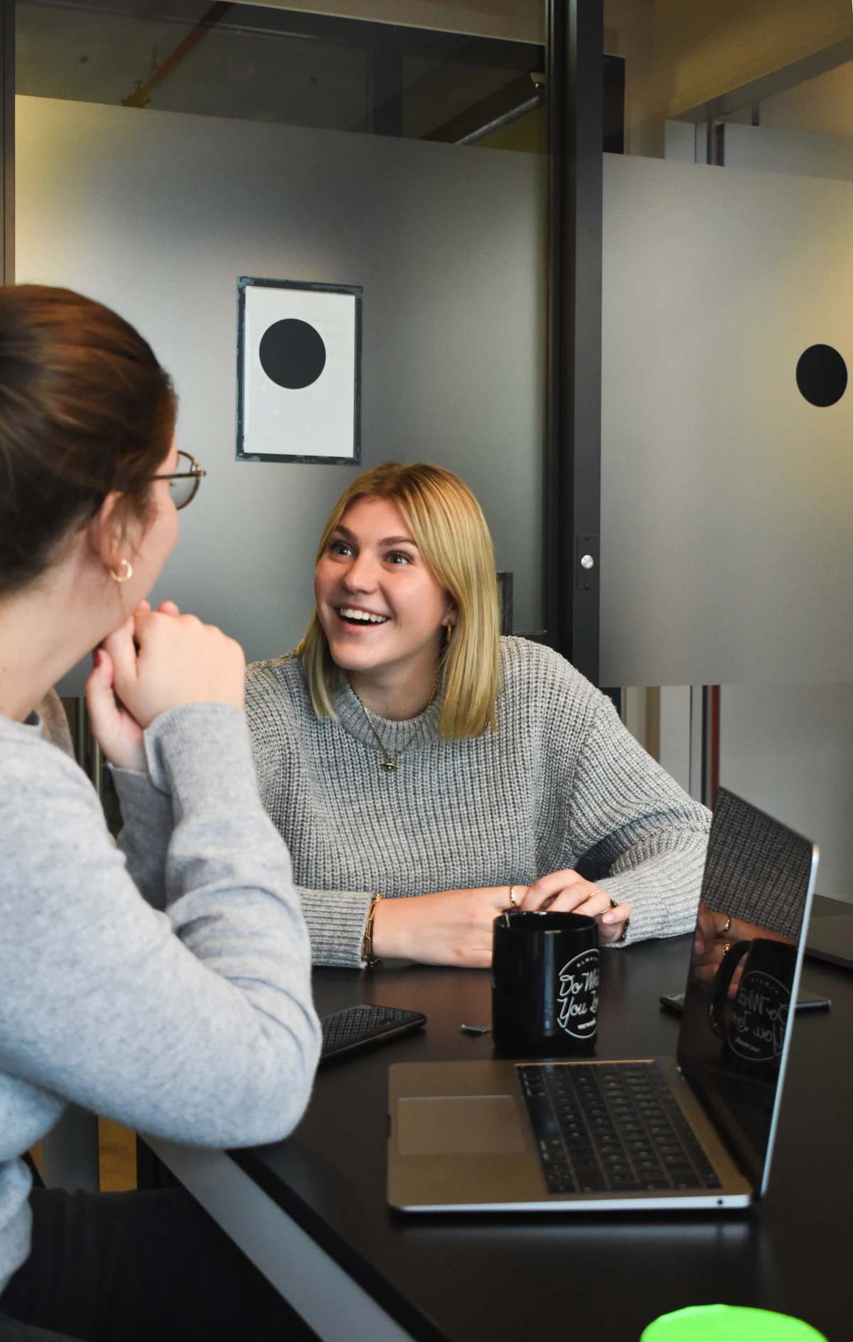 A woman mid-sentence and laughing as she explains something to a colleague across a desk
