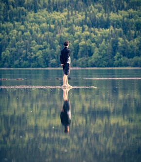 man in black shirt and black shorts standing on brown wooden dock during daytime