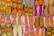 A vibrant array of traditional shoes displayed in an organized grid, featuring intricate embroidery and diverse patterns. The footwear exhibits an array of colors, including vivid pinks, oranges, yellows, and hints of blue, arranged on a flat surface, highlighting the craft and cultural richness.