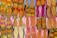 A vibrant array of traditional shoes displayed in an organized grid, featuring intricate embroidery and diverse patterns. The footwear exhibits an array of colors, including vivid pinks, oranges, yellows, and hints of blue, arranged on a flat surface, highlighting the craft and cultural richness.
