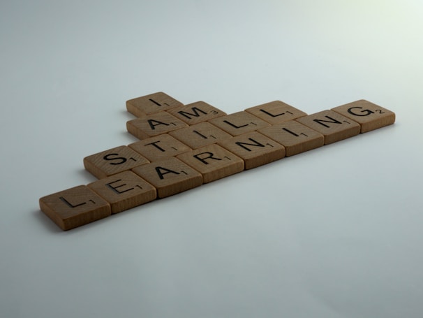 Wooden Scrabble tiles arranged to form the words 'I AM STILL LEARNING' on a flat surface.