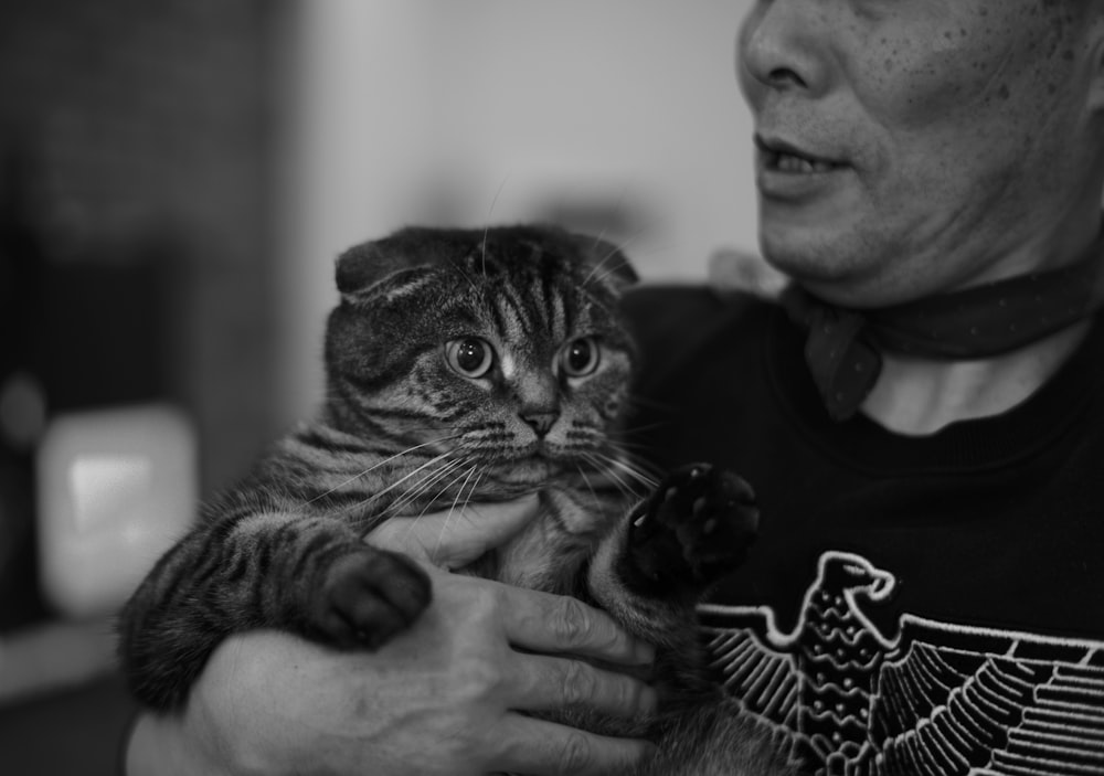 man in black shirt holding brown tabby cat