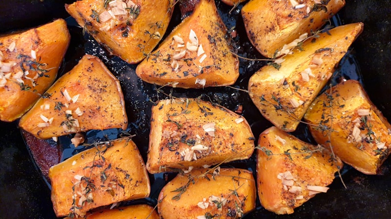 Wedges of roasted pumpkin scattered with herbs and garlic on a dark tray