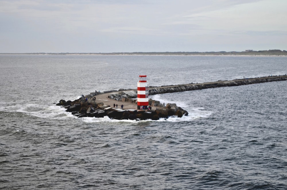 Faro rojo y blanco en formación rocosa marrón en el mar durante el día