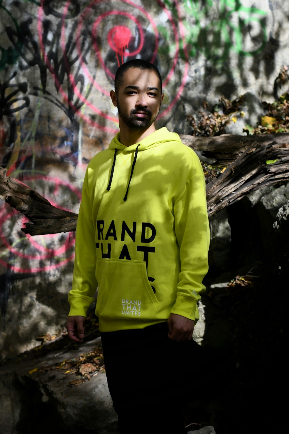 man in yellow and black hoodie standing near brown tree log