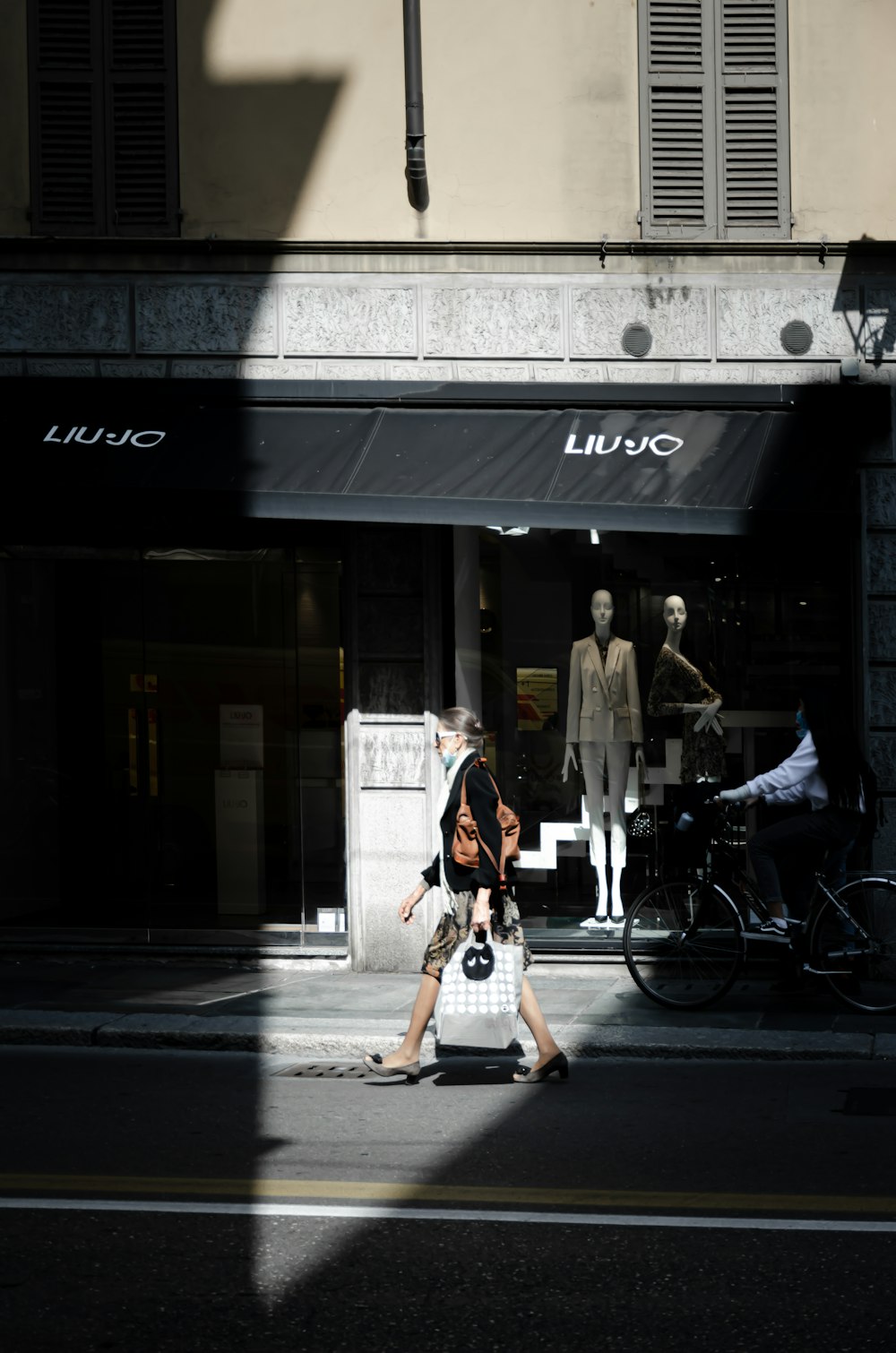 Mann in schwarz-weiß kariertem Hemd und schwarzer Hose, der tagsüber auf dem Bürgersteig spazieren geht