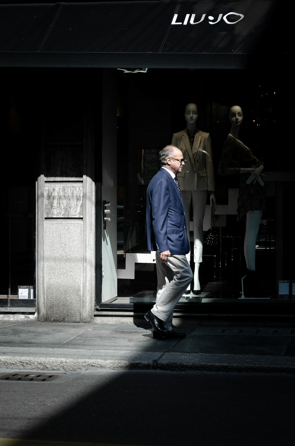 homem em camisa de botão azul e calças brancas andando na calçada durante o dia