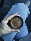 Artistic close-up of a hand adorned with mixed-metal rings holding a coffee cup.