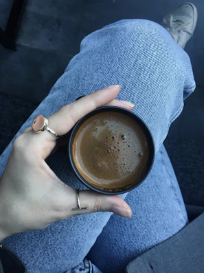 Artistic close-up of a hand adorned with mixed-metal rings holding a coffee cup.