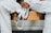 A person dressed in a white martial arts uniform is sitting on a wooden bench holding a white belt. The person's hands have some fingers wrapped with athletic tape.