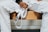 A person dressed in a white martial arts uniform is sitting on a wooden bench holding a white belt. The person's hands have some fingers wrapped with athletic tape.