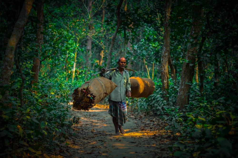 a man walking down a dirt road carrying a barrel