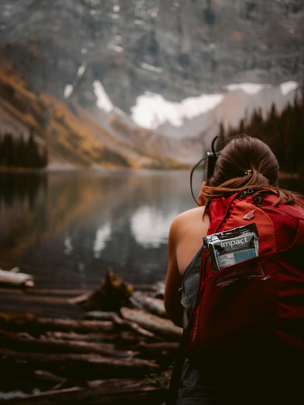 woman in red backpack standing near lake during daytime