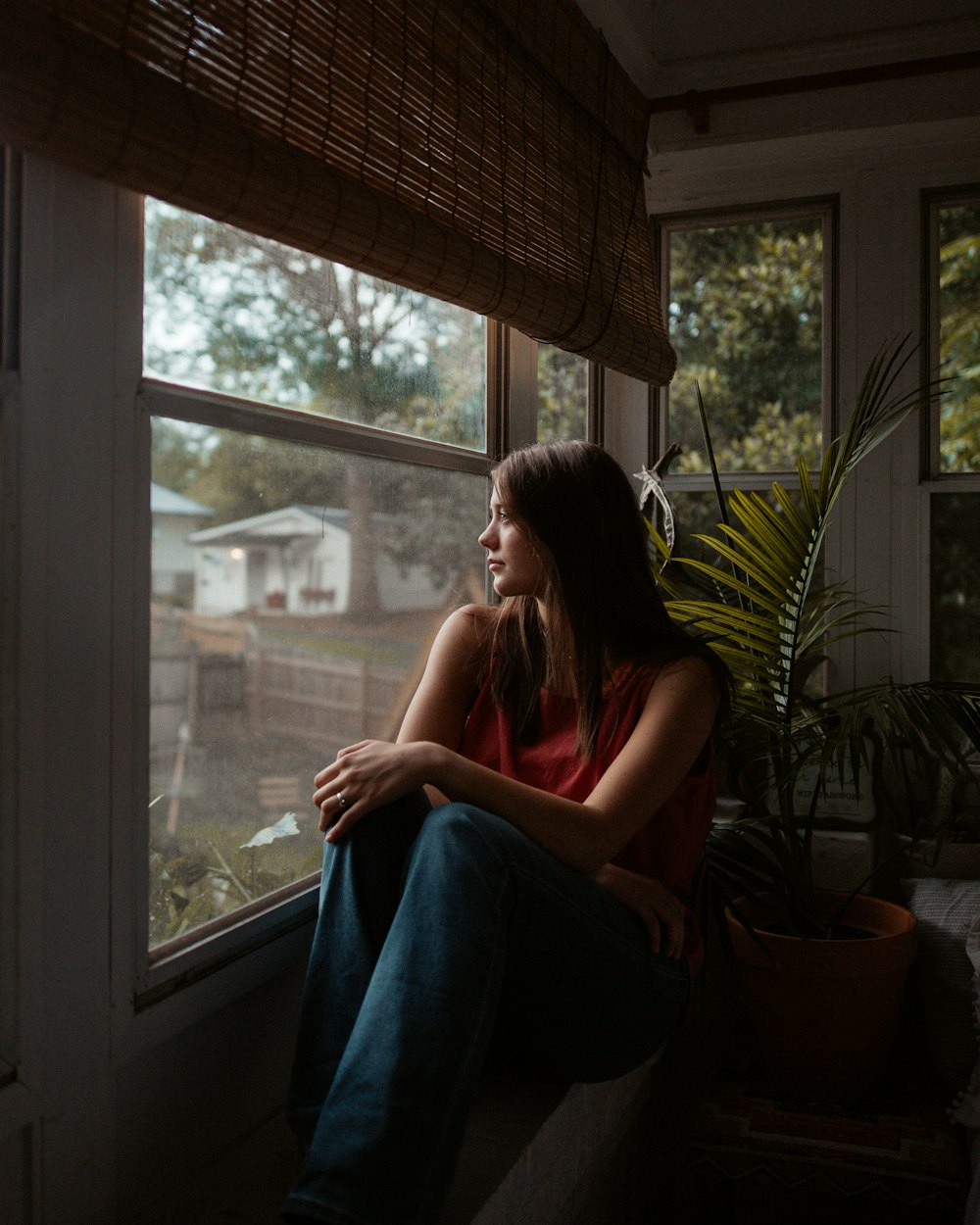 窓辺に座る赤いタンクトップの女性