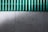 A concrete wall with a green corrugated sheet above it. The wall has a textured surface with visible holes and marks. The corrugated sheet is translucent and contrasts with the wall.