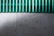 A concrete wall with a green corrugated sheet above it. The wall has a textured surface with visible holes and marks. The corrugated sheet is translucent and contrasts with the wall.