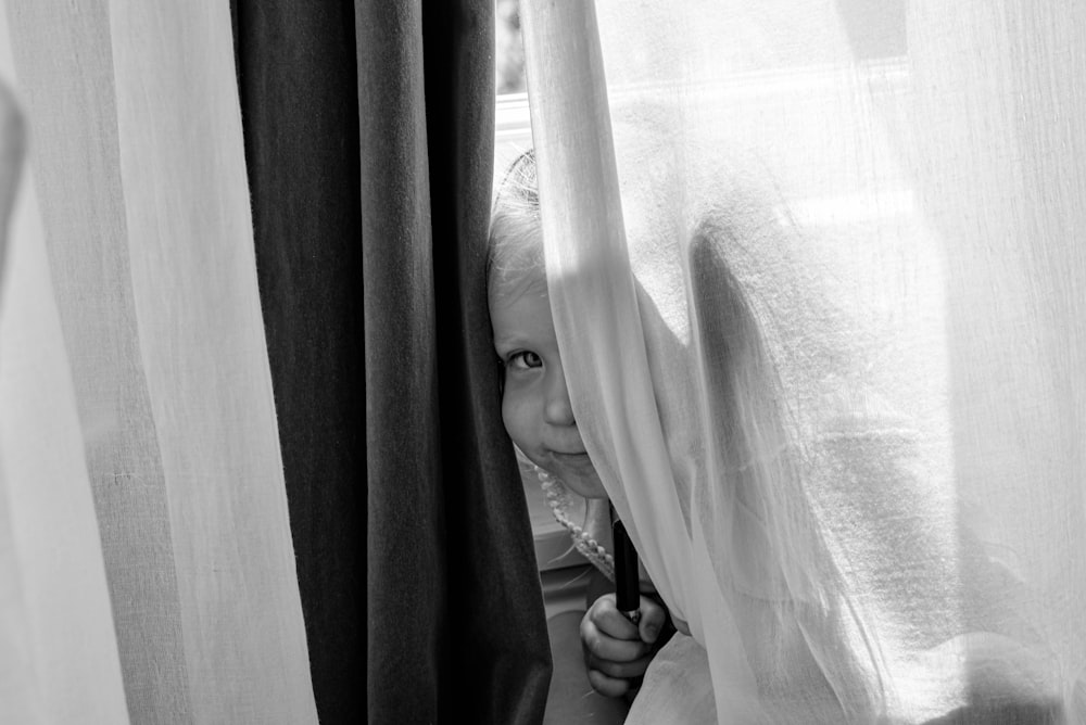 grayscale photo of woman holding curtain