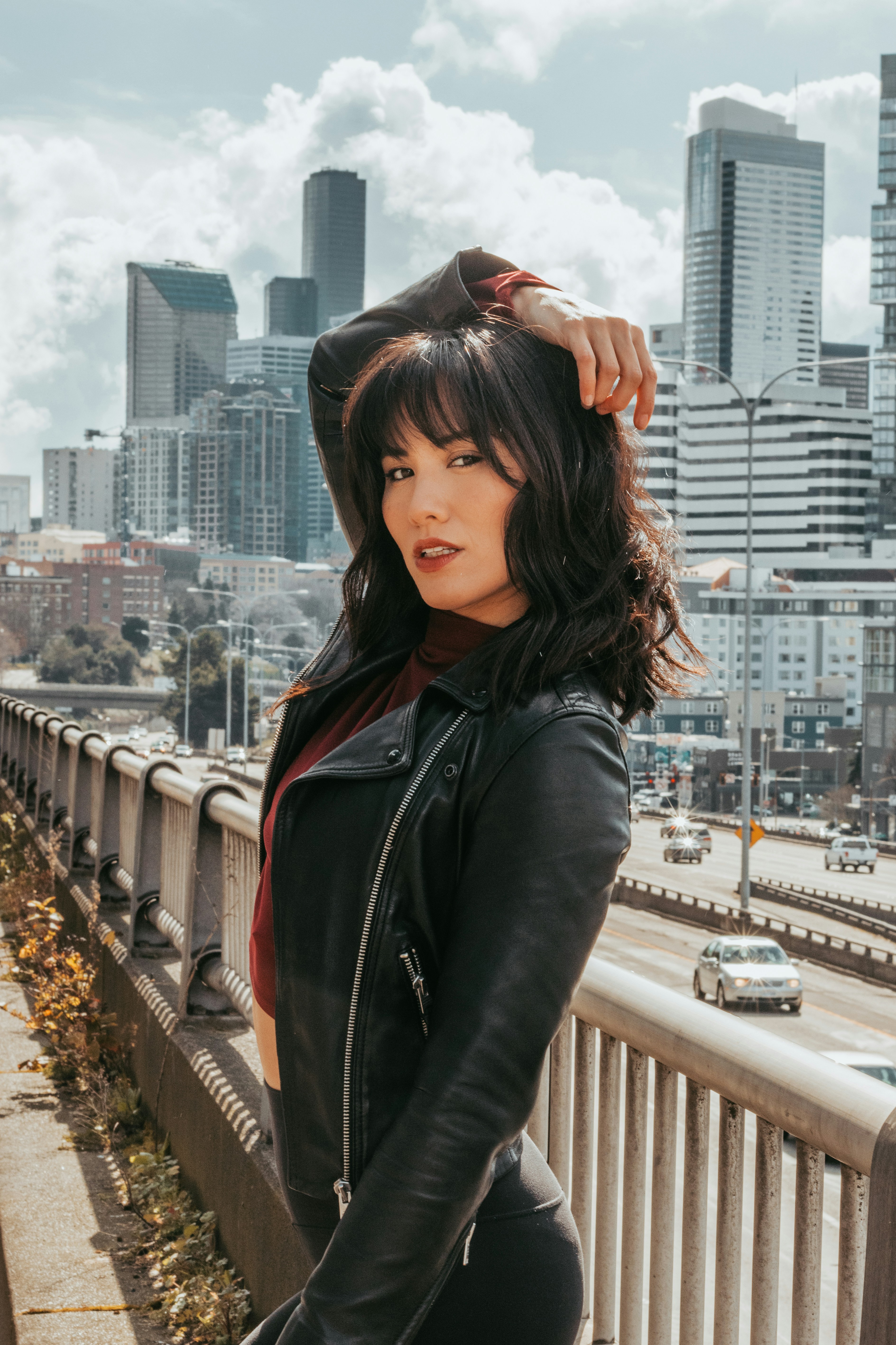wanita dengan jaket kulit hitam berdiri di jembatan di siang hari