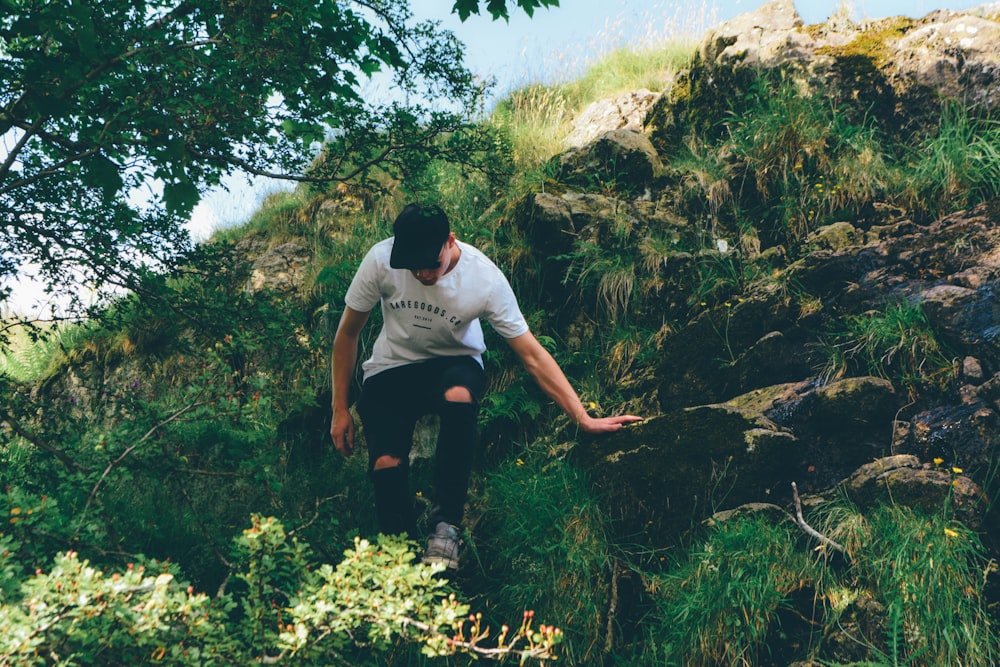 man in white t-shirt and black pants sitting on rock during daytime