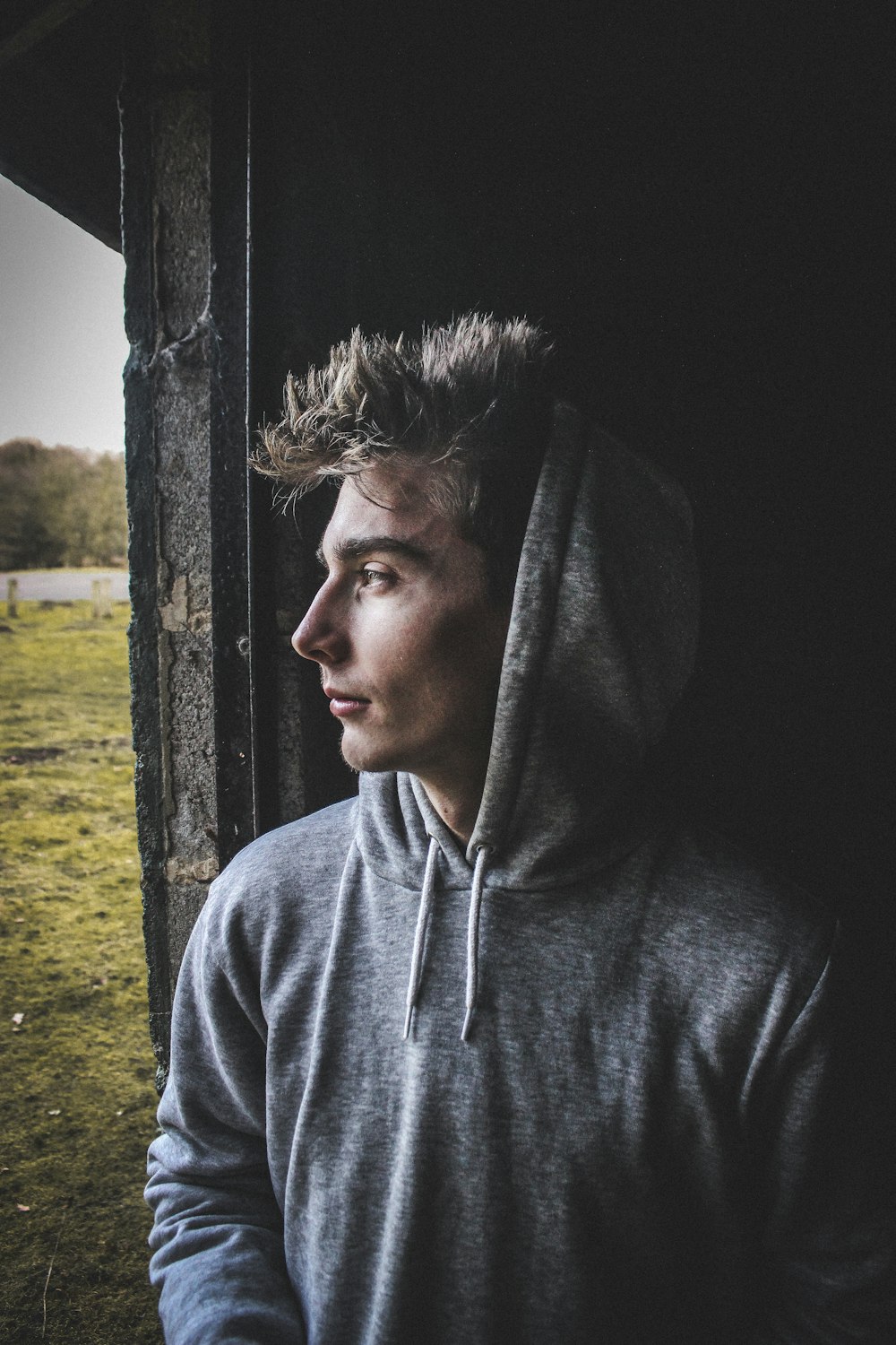 man in gray hoodie standing beside brown wooden post during daytime