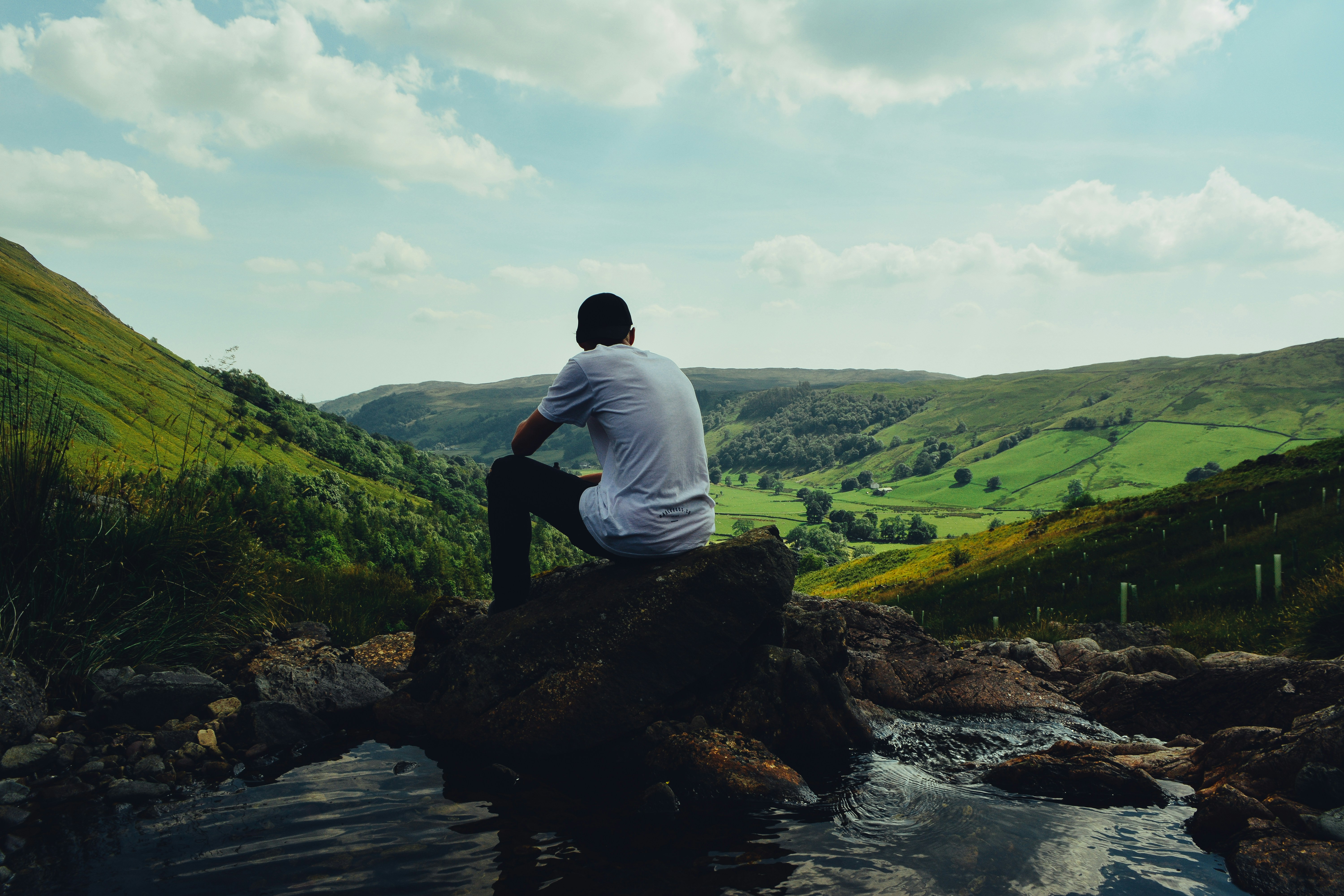 man in white shirt sitting on rock in front of river during daytime