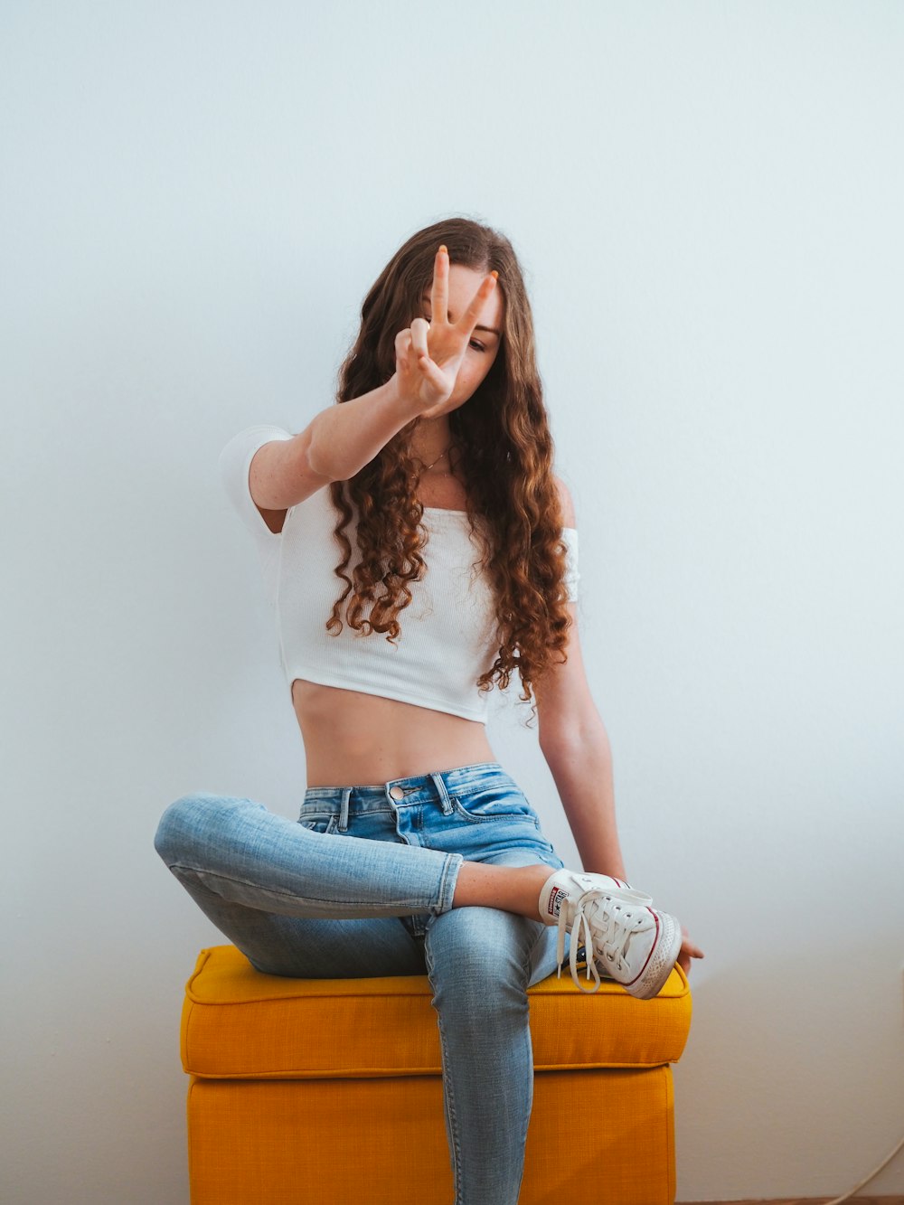 Mujer con camiseta blanca sin mangas y jeans vaqueros azules sentada en una silla amarilla