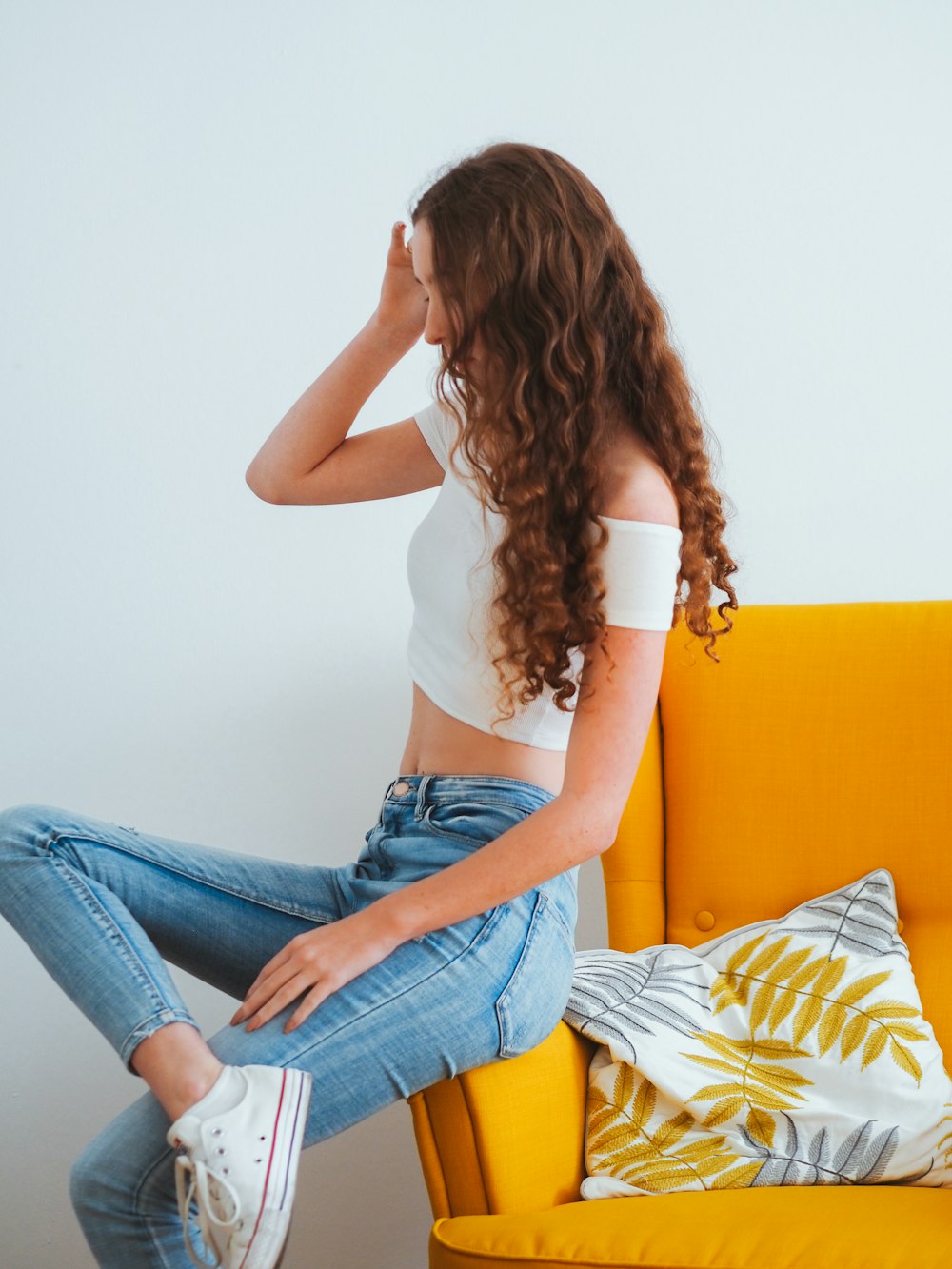 Frau in weißem Tanktop und blauer Jeans sitzt auf gelber Couch