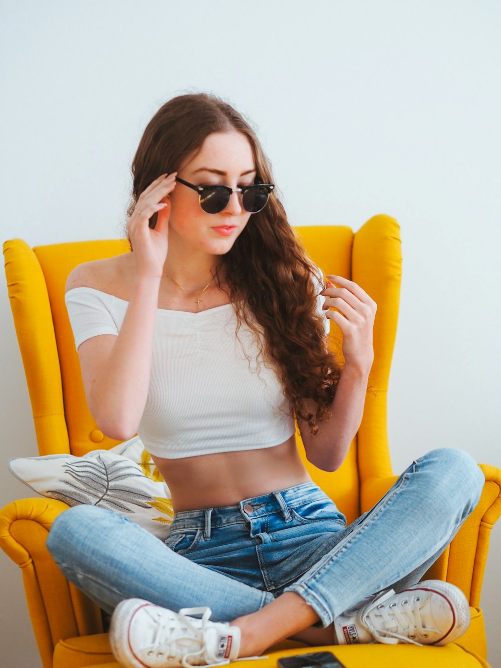 Mujer con camiseta blanca sin mangas y jeans vaqueros azules con gafas de sol negras sentada en cuero amarillo