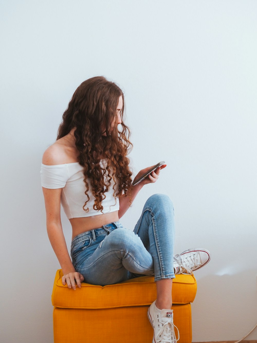 woman in white shirt and blue denim jeans sitting on yellow chair