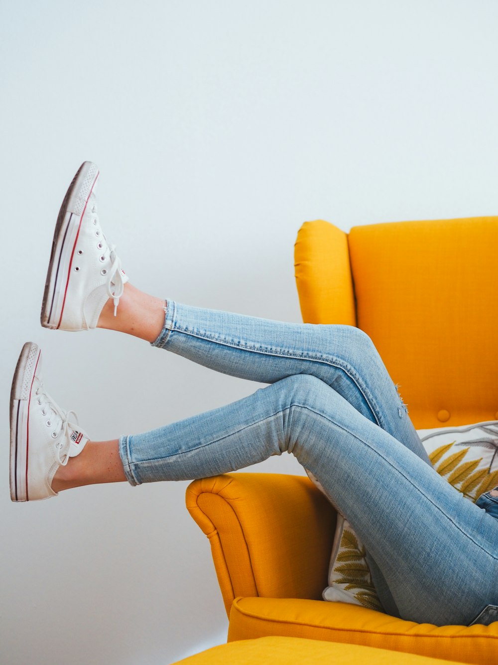 Mujer con jeans de mezclilla azul y zapatillas altas Converse All Star blancas sentadas en naranja