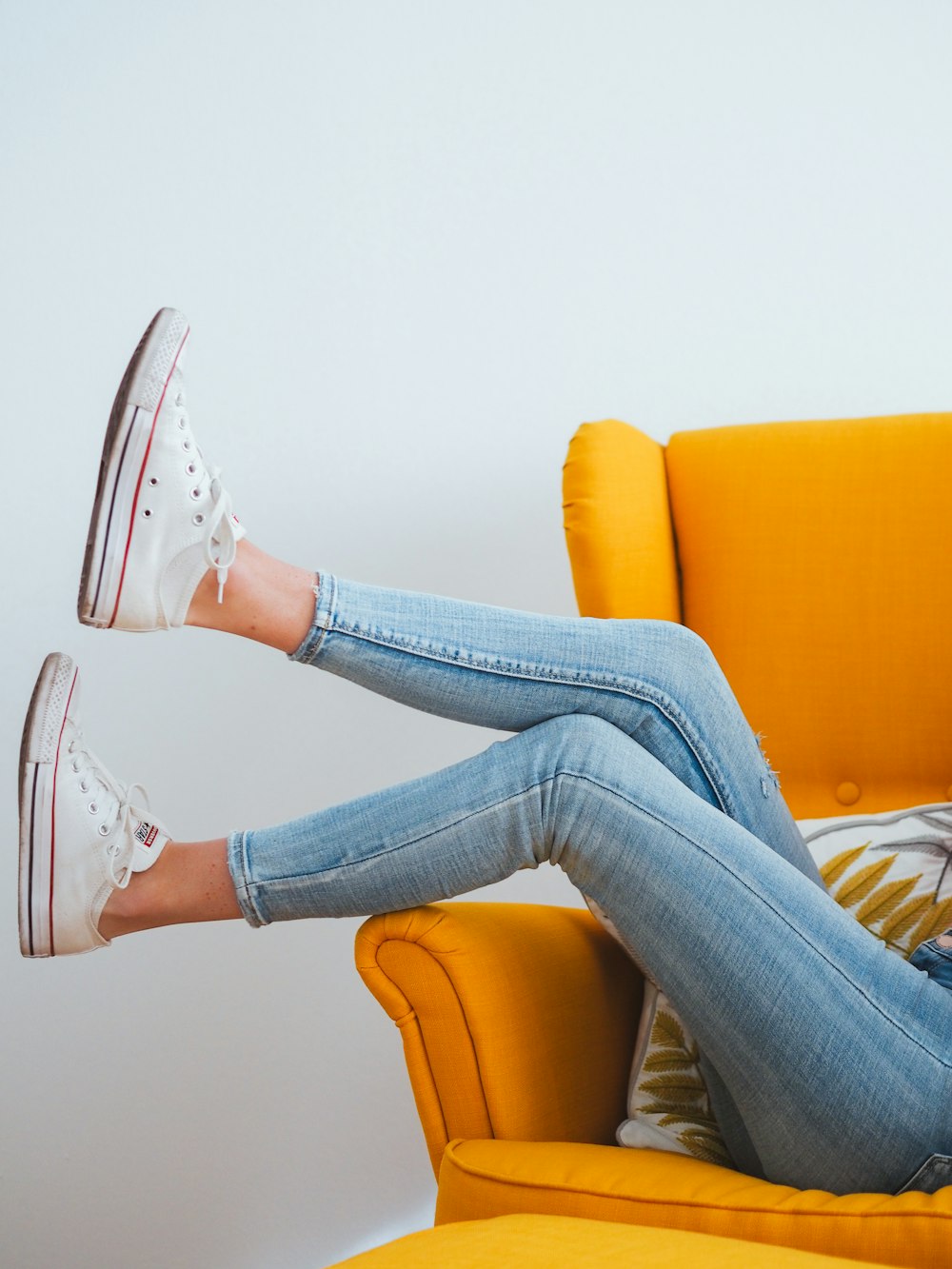 Frau in blauen Jeans und weißen Converse All Star High Top Sneakers sitzt auf Orange